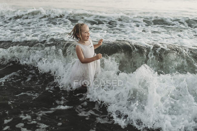 Niña en edad preescolar salpicando en olas al atardecer - foto de stock