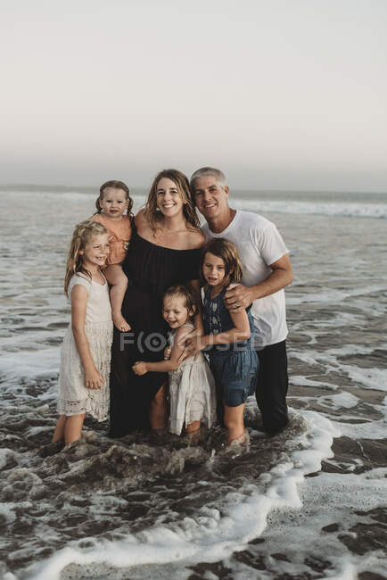 Porträt einer jungen Familie mit nassen Haaren, die bei Sonnenuntergang im Meer steht — Stockfoto