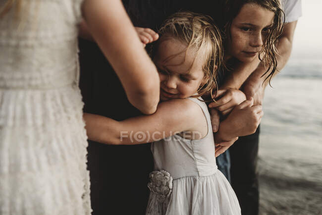 Close up de menina abraçando a família no oceano ao pôr do sol — Fotografia de Stock
