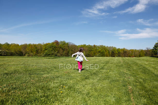 A happy little girl in bright clothing runs through a field in Spring — Stock Photo