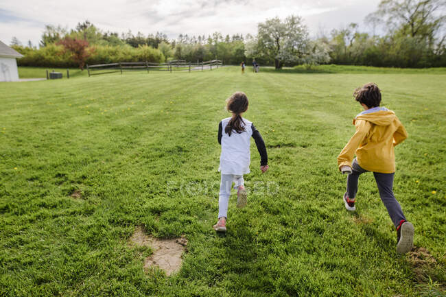 Drei Kinder rennen im Frühling durch ein Feld, eines weit voraus — Stockfoto
