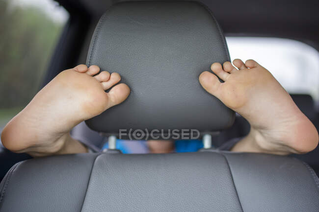 Uma criança no banco de trás de um carro envolve seus pés em volta do banco da frente — Fotografia de Stock