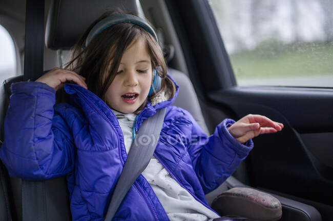 A little girl listens to music on headphones in a car on a car trip — Stock Photo