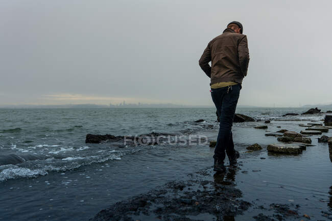 Человек идет по берегу залива с городским силуэтом на горизонте. — стоковое фото