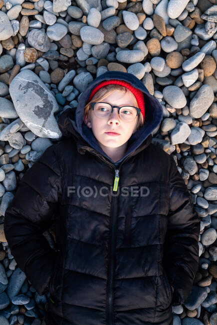 Top down view of tween boy lying on gray and brown stones — Stock Photo