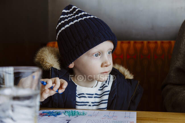 Boy colouring in red restaurant booth wearing white and navy waiting — Stock Photo