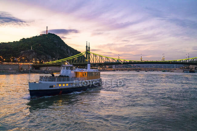 Cruising boat in the danube river with liberty bridge illuminated — Stock Photo