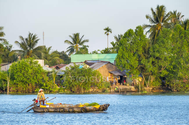 Une femme dans un petit bateau passe devant un village sur la rivière Can Tho, une branche du Mékong, Can Tho, Delta du Mékong, Vietnam — Photo de stock