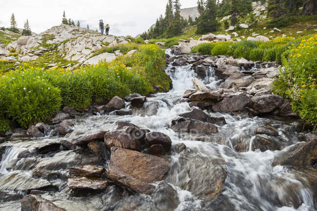 Hikers pass cascade near Pierre Lakes, Elk Mountains, Colorado — Stock Photo