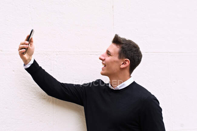 Young urban-looking man raises his cell phone and makes a selfie — Stock Photo