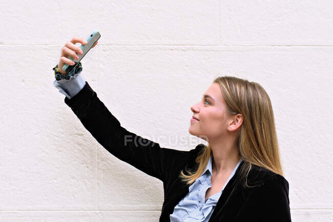 Beautiful modern-looking girl raises her cell phone and makes a — Stock Photo