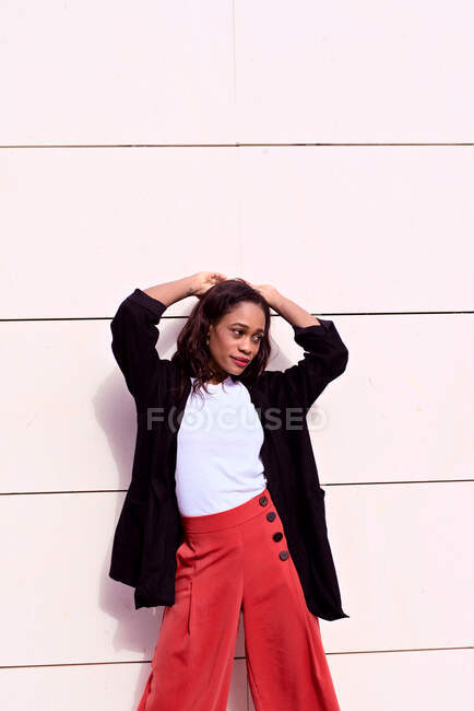 La mujer a la moda joven africana posa en la pared al sol - foto de stock