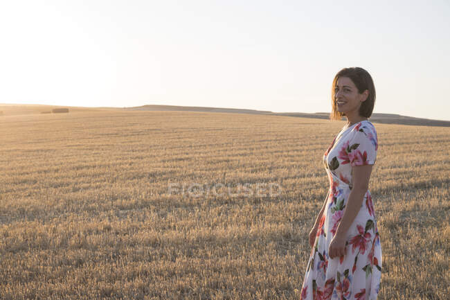 Mulher sorrindo no campo de trigo ao pôr do sol — Fotografia de Stock
