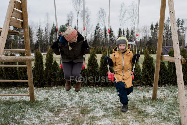 Madre e figlio che giocano su un'altalena insieme fuori nella neve — Foto stock