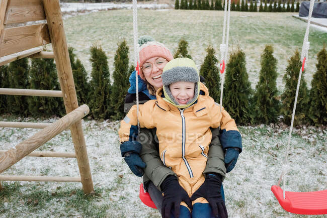 Madre e figlio ridendo oscillando su un'altalena insieme fuori — Foto stock