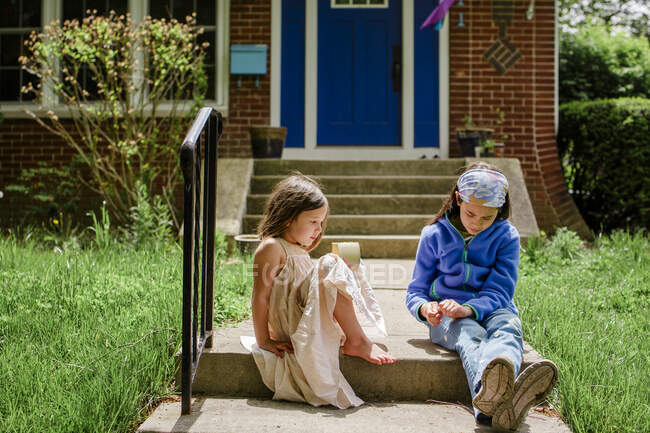 Two little girls sit on front stoop in sunshine talking to each other — Stock Photo