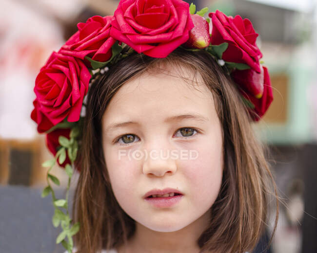 Retrato de una niña seria con una corona de rosas en el pelo - foto de stock