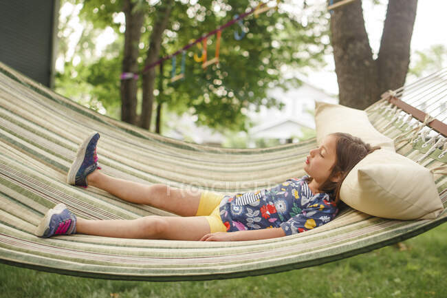 A little girl lays on a hammock by self in sunshine with closed eyes — Stock Photo