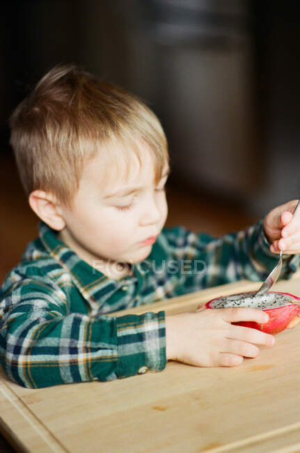 Filmfoto eines kleinen Jungen, der mit einem Löffel eine Drachenfrucht isst. — Stockfoto