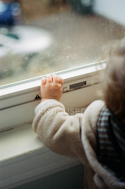 Una niña tocando una ventana. - foto de stock