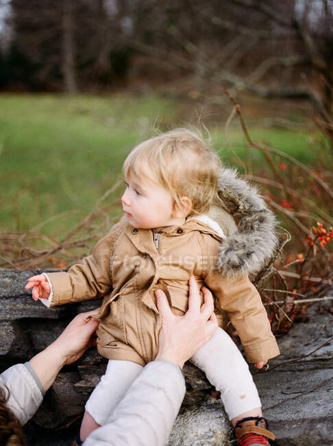 Pequena menina sentada em uma parede de pedra. — Fotografia de Stock