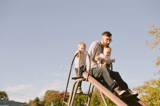 Um pai deslizando com seus filhos em um playground. — Fotografia de Stock