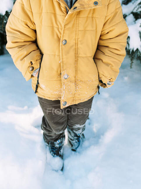 Малюк стоїть на снігу з яскраво-жовтим піджаком . — стокове фото
