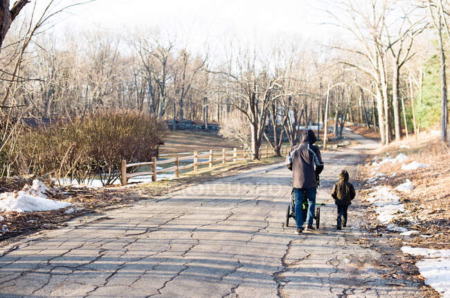 Un padre y un hijo en un paseo con un bebé en un cochecito. - foto de stock