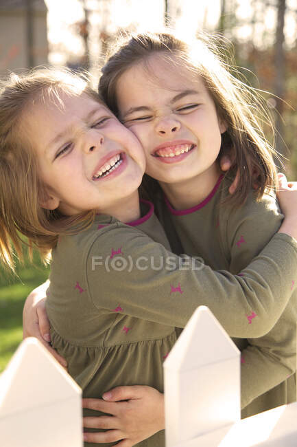 Hermanas abrazándose al sol sonriendo - foto de stock