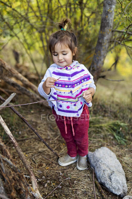 Smiley süßes kleines Mädchen mit einem Holzstock im Wald stehend — Stockfoto