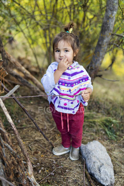 Sorridente carina bambina che tiene in mano un bastone di legno in piedi nella foresta — Foto stock