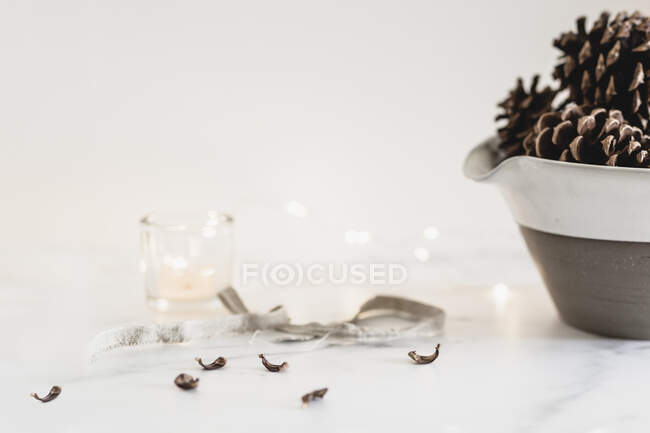 Still life pine cones in stoneware bowl with mini lights, candle — Stock Photo