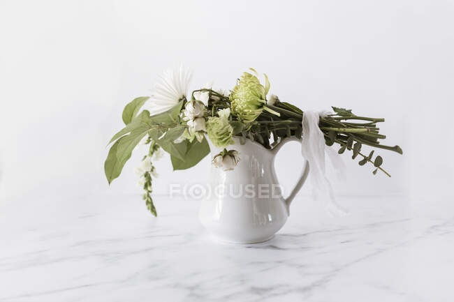 Flower bouquet tied with linen ribbon laying on top of white pitcher — Stock Photo