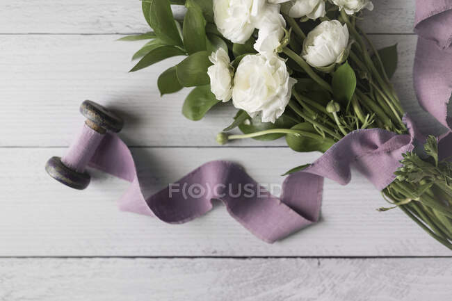 Flores blancas atadas con cinta de lino malva colocada sobre tablas blancas - foto de stock