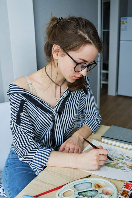 Millennial chica dibuja fabulosas imágenes en papel mientras se sienta en casa - foto de stock