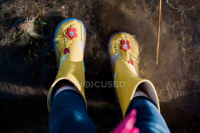 Kinderfüße in Regenstiefeln in einer Pfütze aus Wasser und Schlamm — Stockfoto