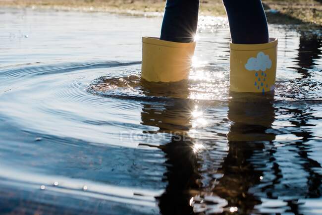 Bottes de pluie pour enfants dans une grande flaque d'eau au coucher du soleil — Photo de stock