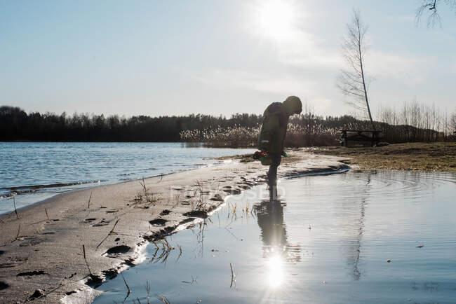 Мальчик играет в воде на солнечном пляже зимой — стоковое фото