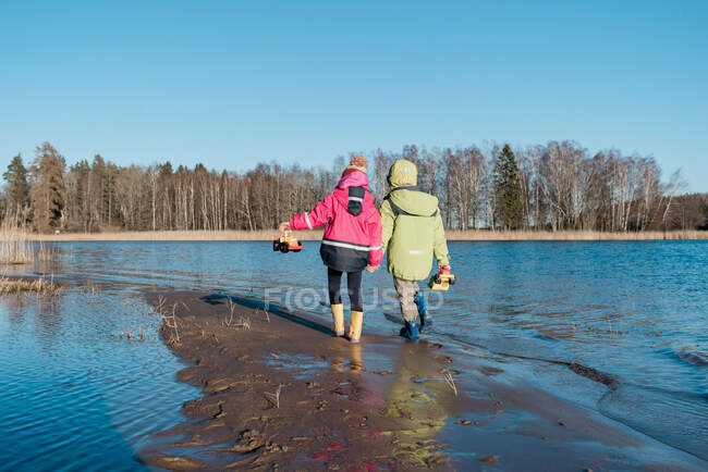 Frères et sœurs se tenant la main en marchant sur la plage par une journée ensoleillée — Photo de stock