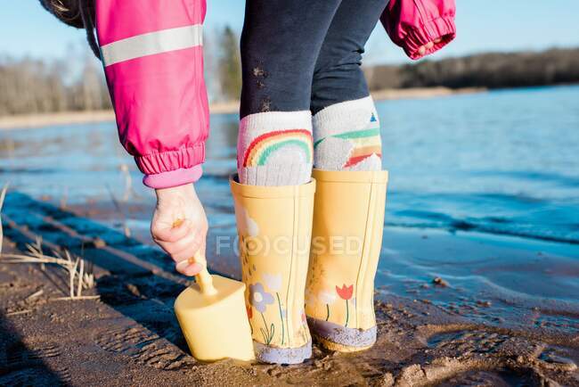 Stivali da pioggia per bambini e vanga su una spiaggia sotto il sole — Foto stock