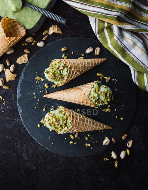 Crème glacée dans des cônes de gaufre avec pistache sur un fond sombre. vue de dessus. — Photo de stock
