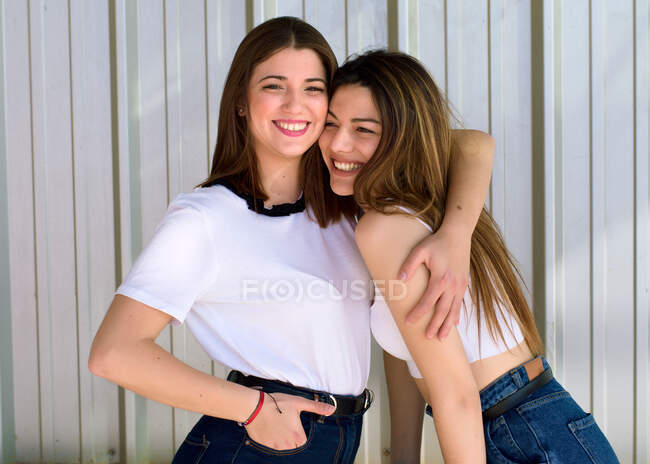 Dos jóvenes amigos abrazan y ríen felizmente mirando a la cámara - foto de stock