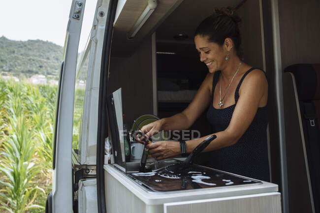 Woman with earrings washing dishes in motorhome during a vacation. — Stock Photo