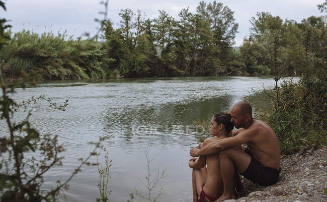Pareja en trajes de baño abrazándose por una orilla del río durante unas vacaciones. - foto de stock