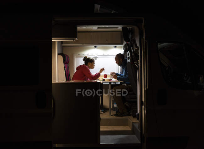 Pareja teniendo una cena relajada en una autocaravana durante un viaje. - foto de stock