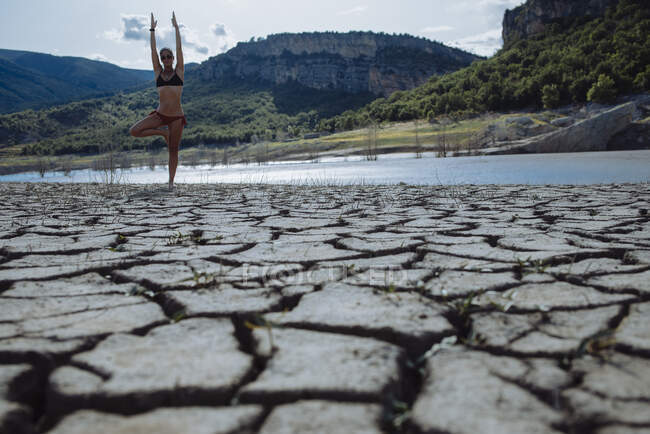 Frau balanciert auf einem Bein am Ufer eines Sees. — Stockfoto