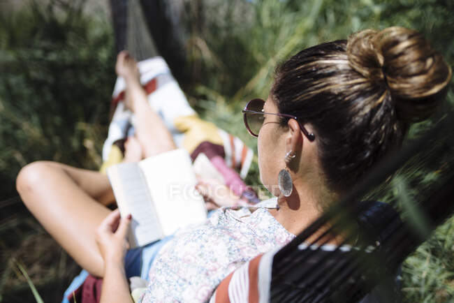 Женщина в солнечных очках читает книгу, лежащую на гамаке. — стоковое фото