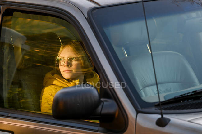 Хлопчик сидить у машині, дивлячись на вікно воріт, що встановлює сонце — стокове фото