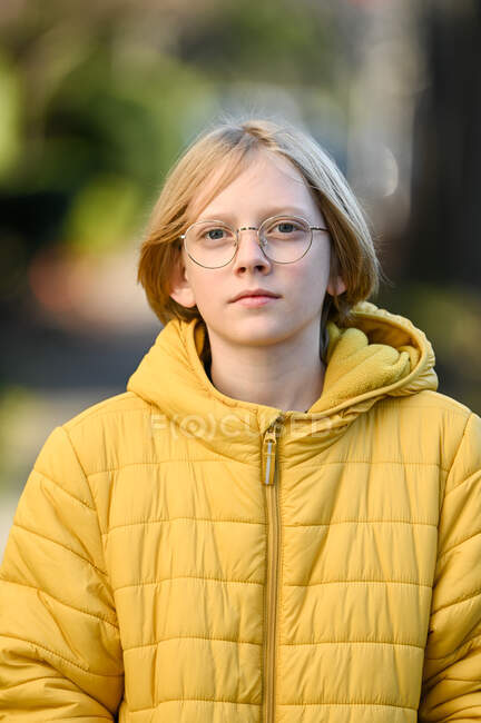 Tween menino com óculos e casaco amarelo sorrindo olhando para a câmera — Fotografia de Stock