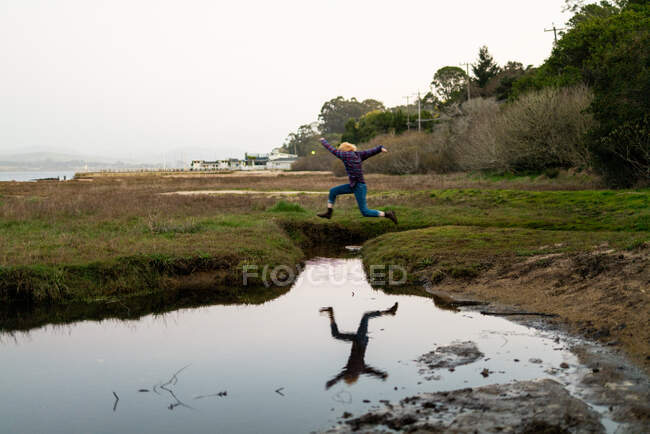 Teen jumping over inlet of pool of still water casting reflection. — Stock Photo